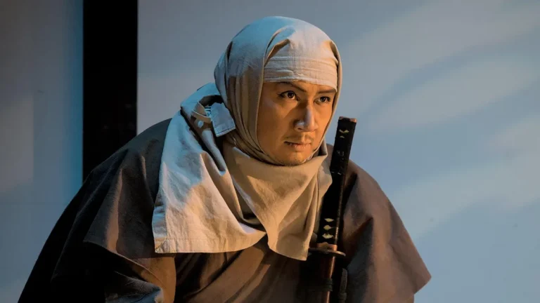 Japanese actor in a light headscarf holding a katana, looking off-camera.