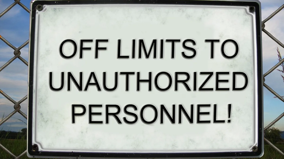 A white sign with black text reading 'OFF LIMITS TO UNAUTHORIZED PERSONNEL!' mounted on a chain-link fence.