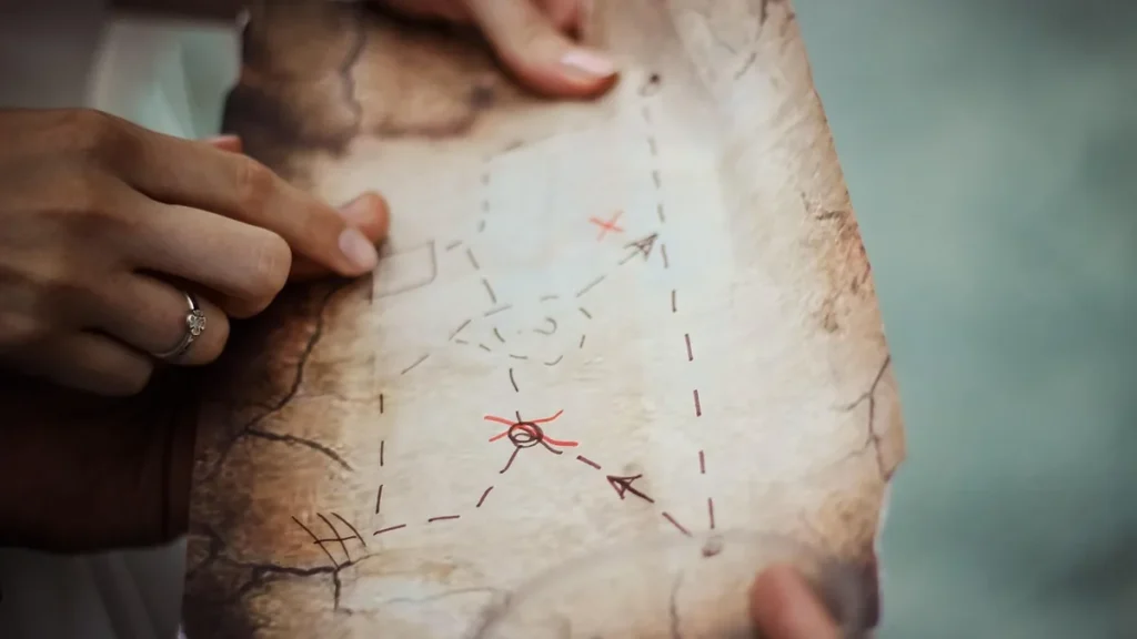 Hands holding and pointing at a parchment map with hand-drawn routes and red crosses.