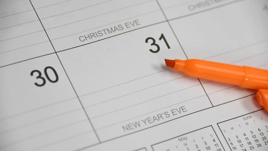 Orange marker resting on a calendar page displaying the dates 30 and 31 with holiday labels.