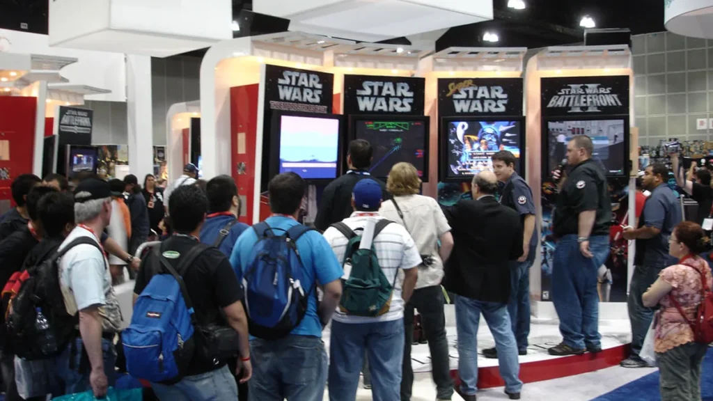 Crowd gathered around Star Wars game kiosks, including Super Star Wars and Battlefront II, at a convention.