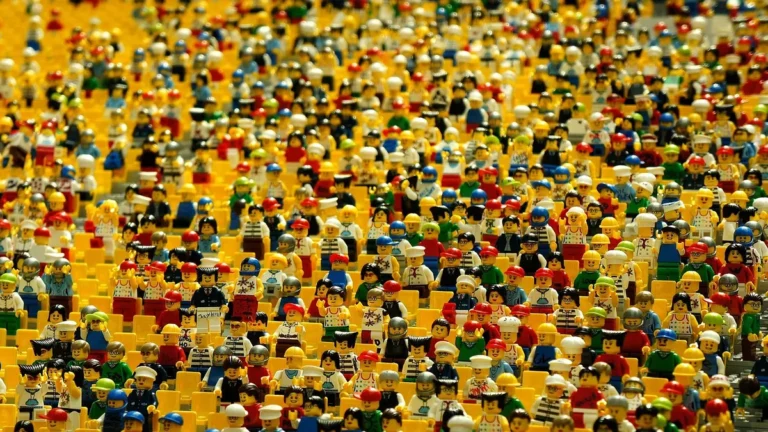 A dense crowd of colorful Lego minifigures sitting in rows of yellow seats.
