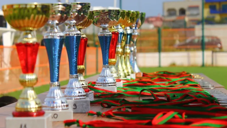 Row of colorful trophies with red and green ribbons lined up on a table, symbolizing tournament victory and awards.