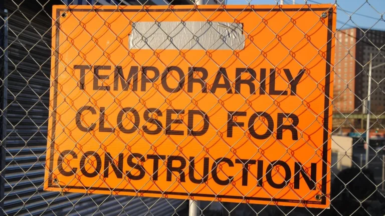 Orange sign behind a chain-link fence reading 'Temporarily Closed for Construction'.