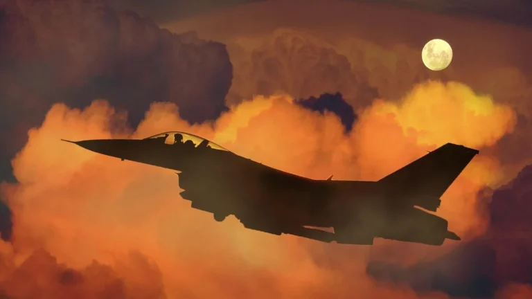 Silhouette of a fighter jet flying through orange clouds under a full moon.