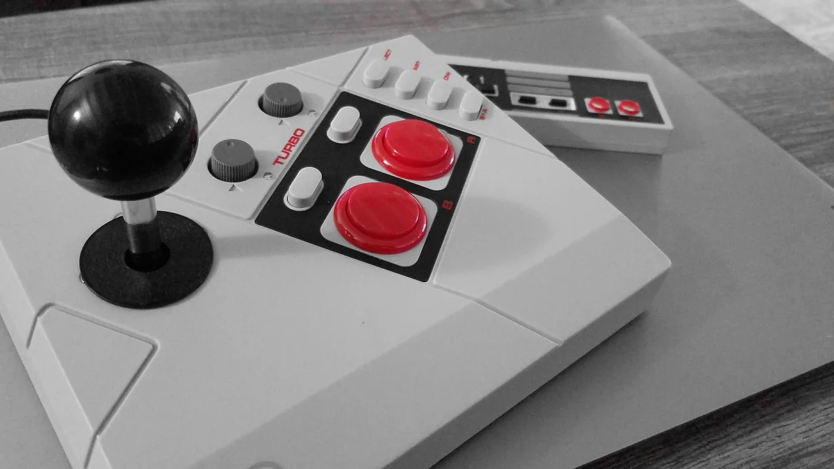 White retro arcade joystick with bright red buttons, alongside a classic grey NES controller.