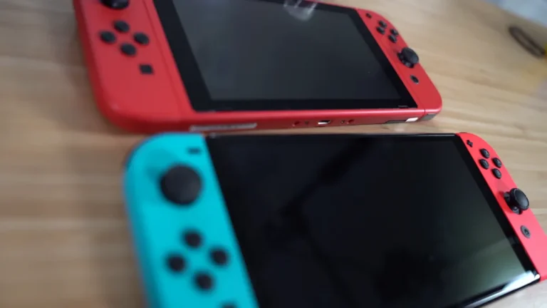Two Nintendo Switch consoles, one red and one with blue and red Joy-Cons, resting on a wooden table.
