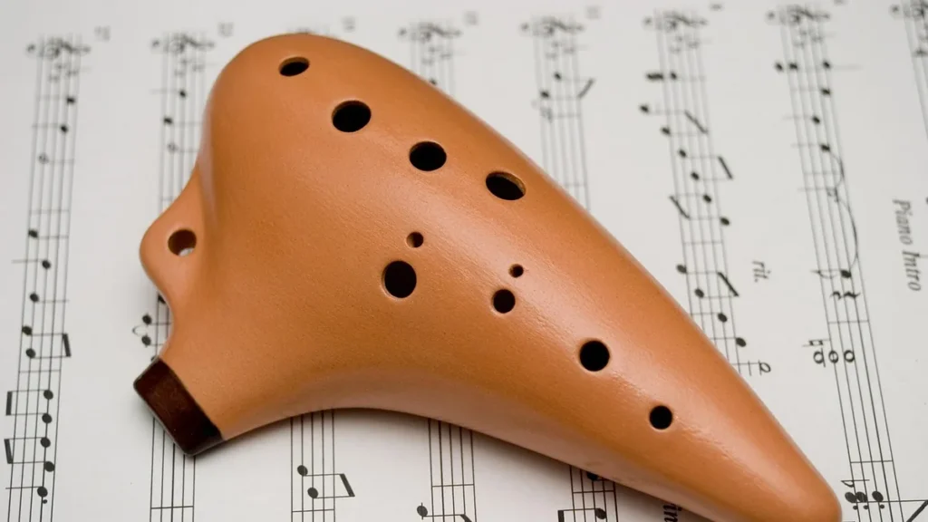 A brown clay ocarina with multiple finger holes rests on a sheet of music.