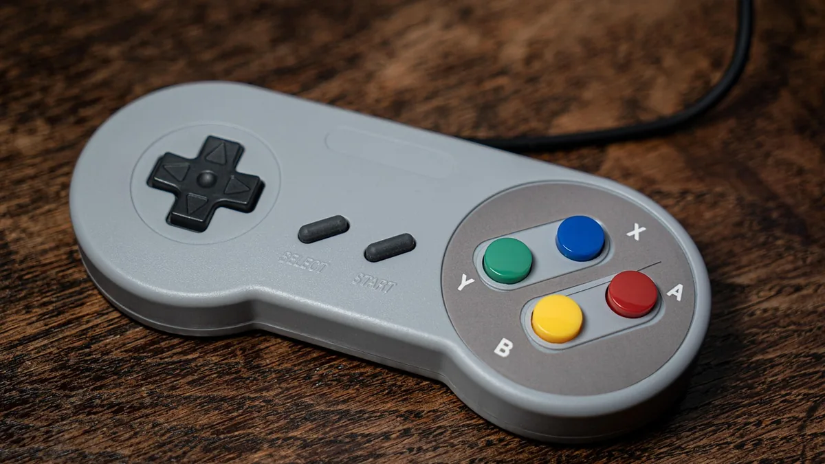 Grey retro-style game controller with colorful A, B, X, Y buttons resting on a dark wooden surface.