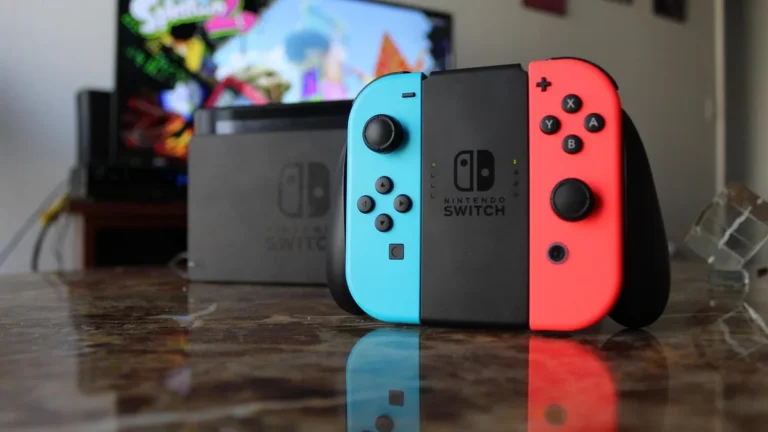 Neon blue and red Nintendo Switch Joy-Con controllers mounted on a grip, with a colorful game display blurred on a TV in the