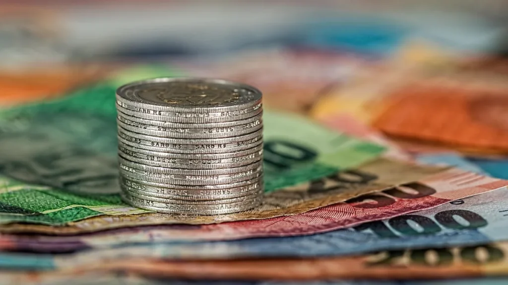 Stack of silver coins on colorful banknotes, symbolizing money, refunds, and financial transactions.