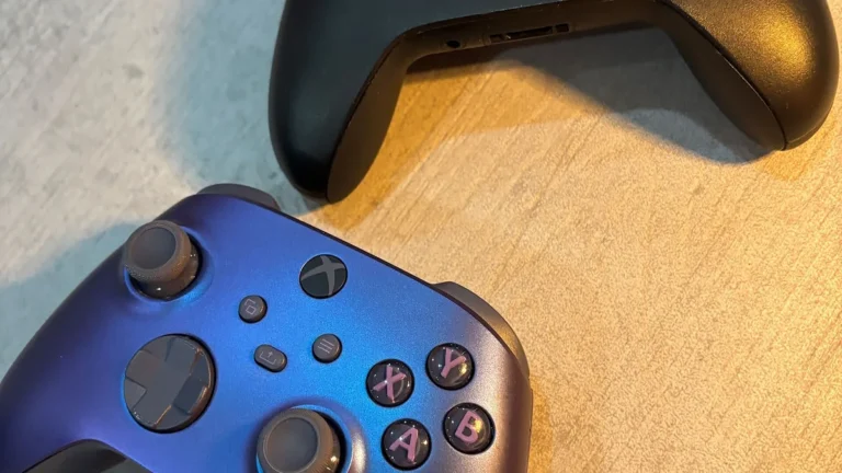 A close-up of a metallic blue Xbox controller next to a black controller on a wooden surface.