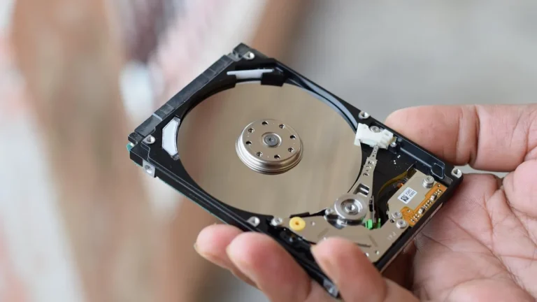 Hand holding an open hard drive showing the shiny metallic platter and internal read-write mechanism.