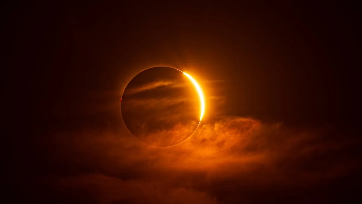 A glowing orange solar eclipse shines through dark clouds, evoking cosmic power.