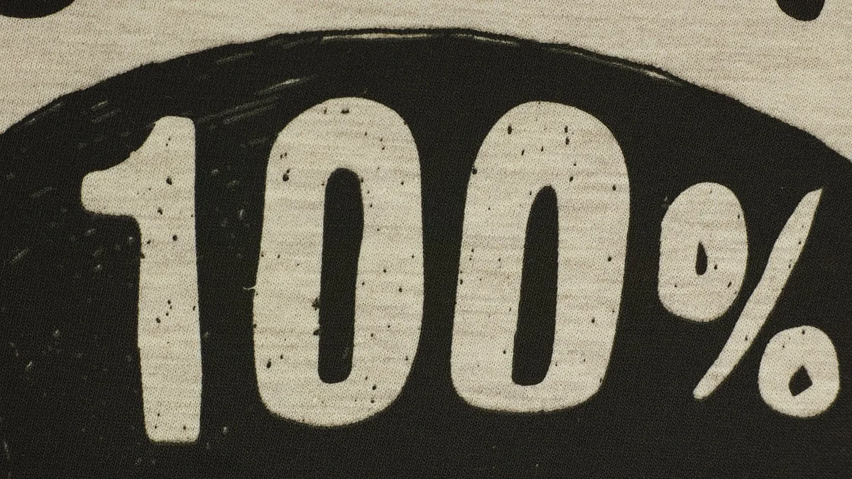 Stylized white text '100%' printed on a black circular background on textured fabric.