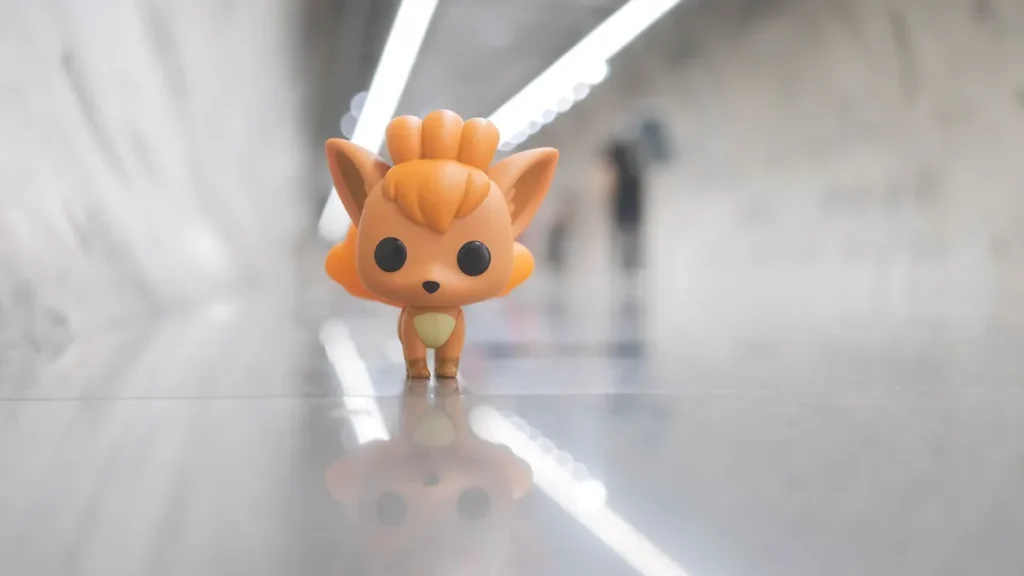 A stylized orange Vulpix figure stands on a reflective surface, representing the Pokémon franchise affected by recent