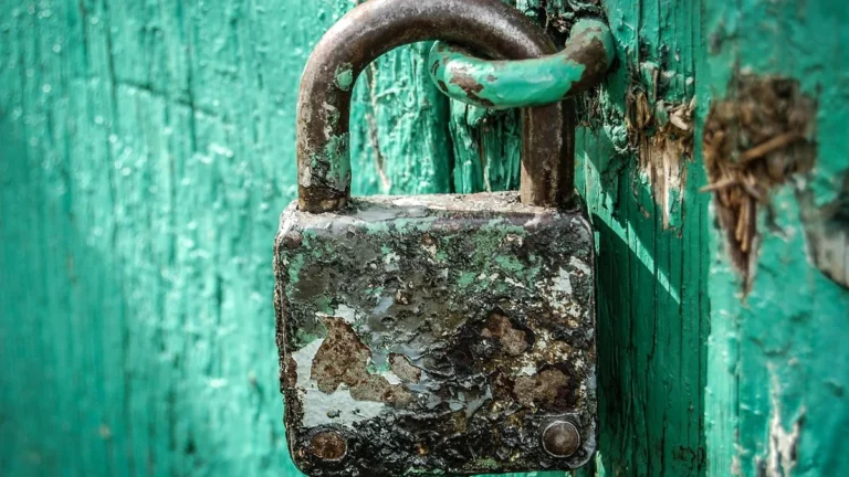 A close-up of a heavily rusted, weathered padlock on a peeling green wooden surface.