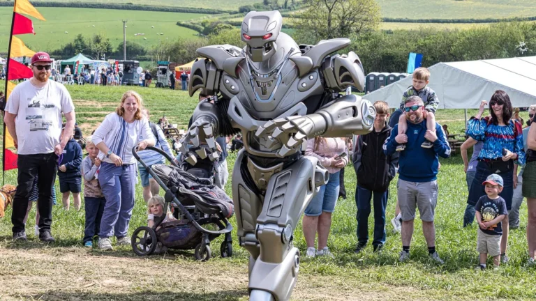 Silver robot costume standing amongst a crowd of onlookers at an outdoor festival.
