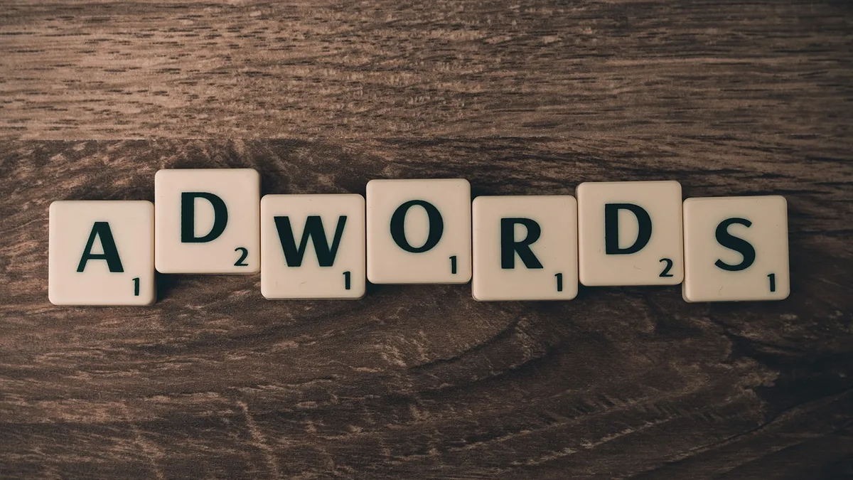 White letter tiles spelling the word ADWORDS on a dark wooden surface.