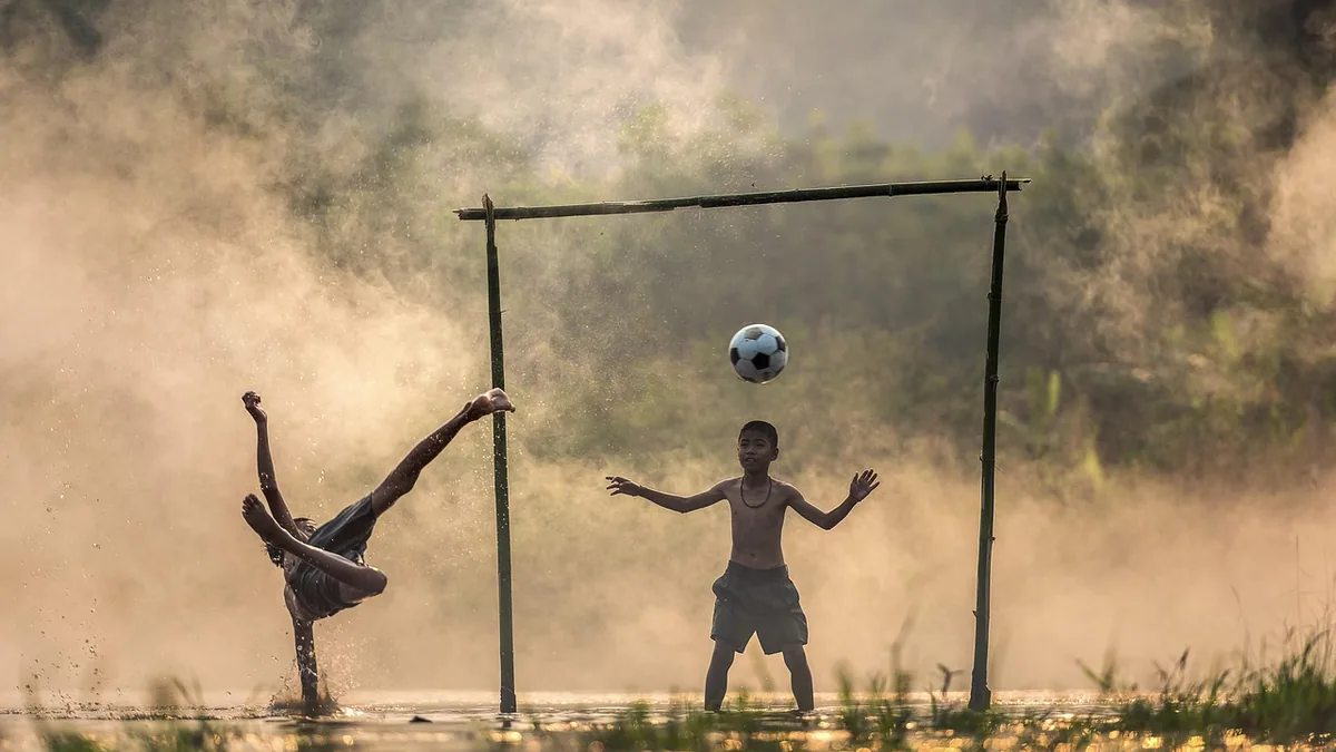 Kids playing soccer in a misty wetland, one performing a bicycle kick with dramatic water splashes.