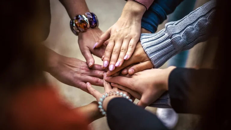 A group of people stacking their hands together in a circle, symbolizing unity and teamwork.