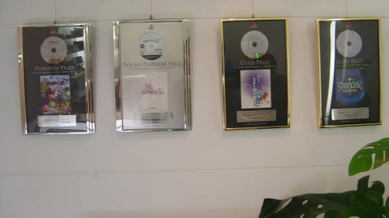 Framed PlayStation sales awards, including Platinum and Gold prizes, hanging on a white wall.