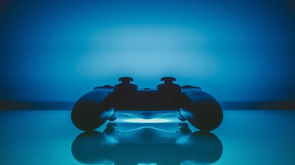 A game controller silhouetted against vibrant blue light, casting a reflection on a glossy surface.