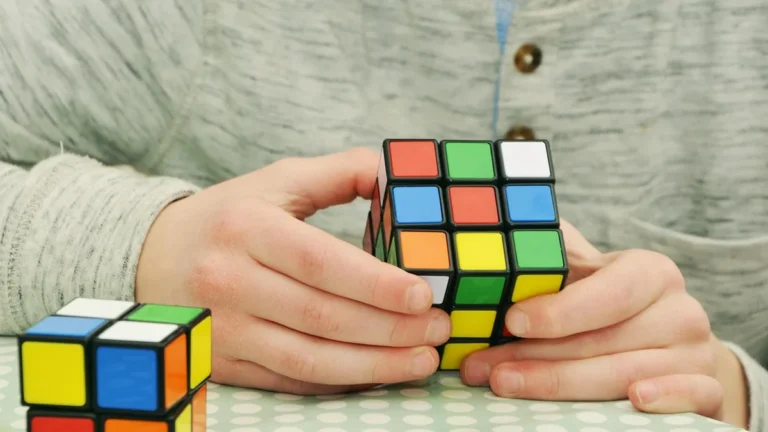 Hands holding a colorful Rubik's cube on a green polka dot table surface.