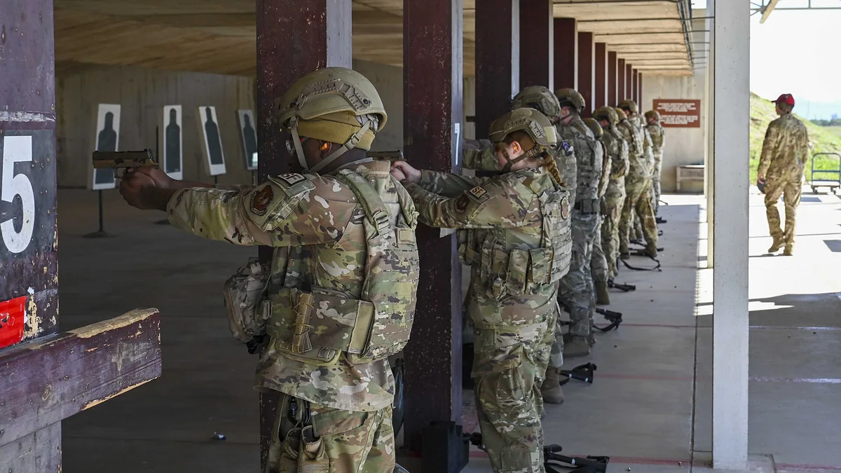 Soldiers in camouflage uniforms aim handguns at targets on a covered shooting range during training.