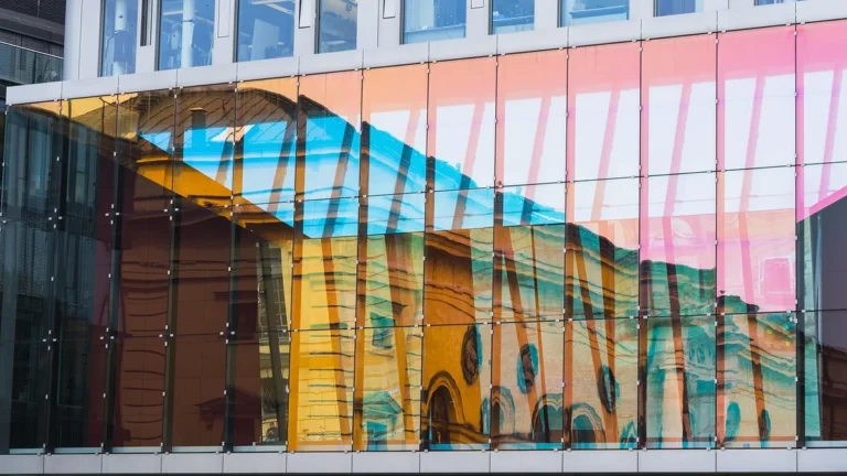 Colorful glass facade of a modern office building reflecting an older yellow building.