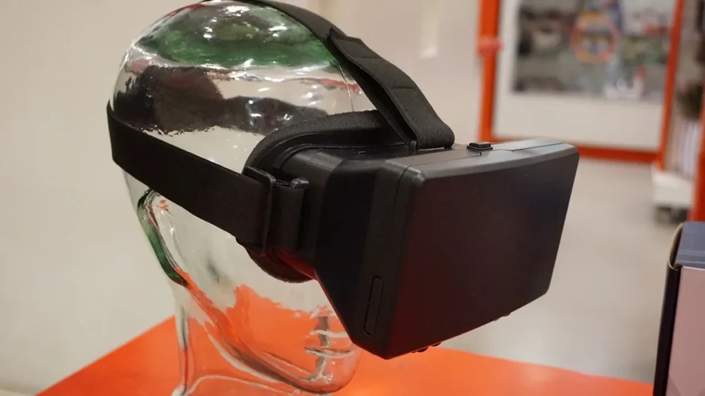 A black virtual reality headset mounted on a transparent glass head model on an orange surface.