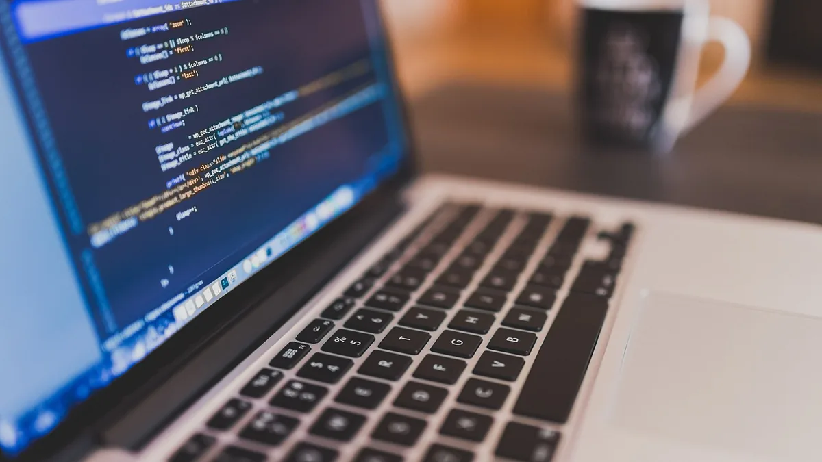 Laptop screen showing lines of code with keyboard in foreground and blurred mug in background.