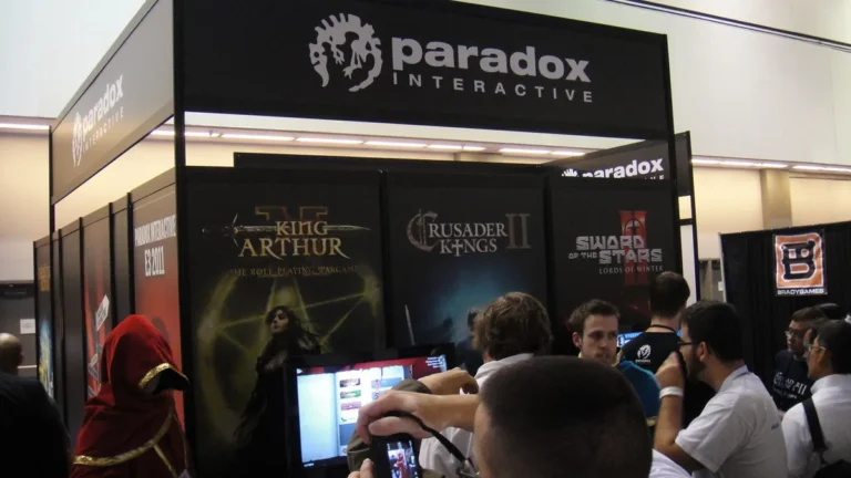 A crowd gathers around the Paradox Interactive booth showcasing posters of their games at a convention.