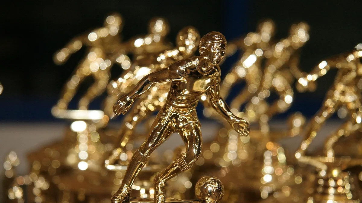 Golden trophies of a soccer player kicking a ball, lined up with a shallow depth of field.