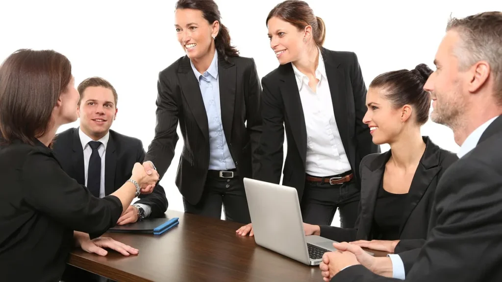 Corporate business professionals shaking hands and collaborating around a conference table with a laptop.