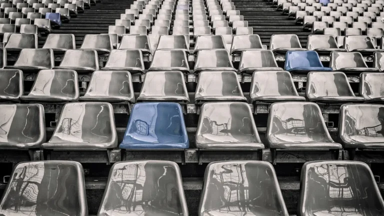 Rows of glossy grey stadium seats with a few highlighted in vibrant blue, reflecting an empty arena.