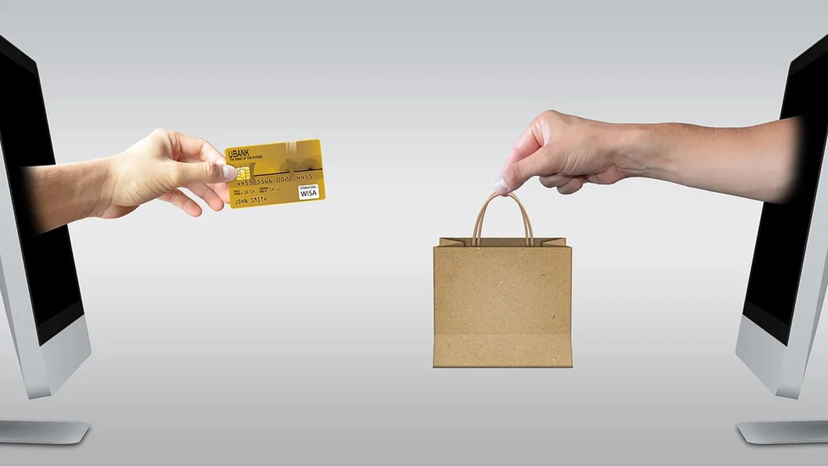 Hands emerge from computer screens, one holding a gold credit card and the other holding a brown paper shopping bag.