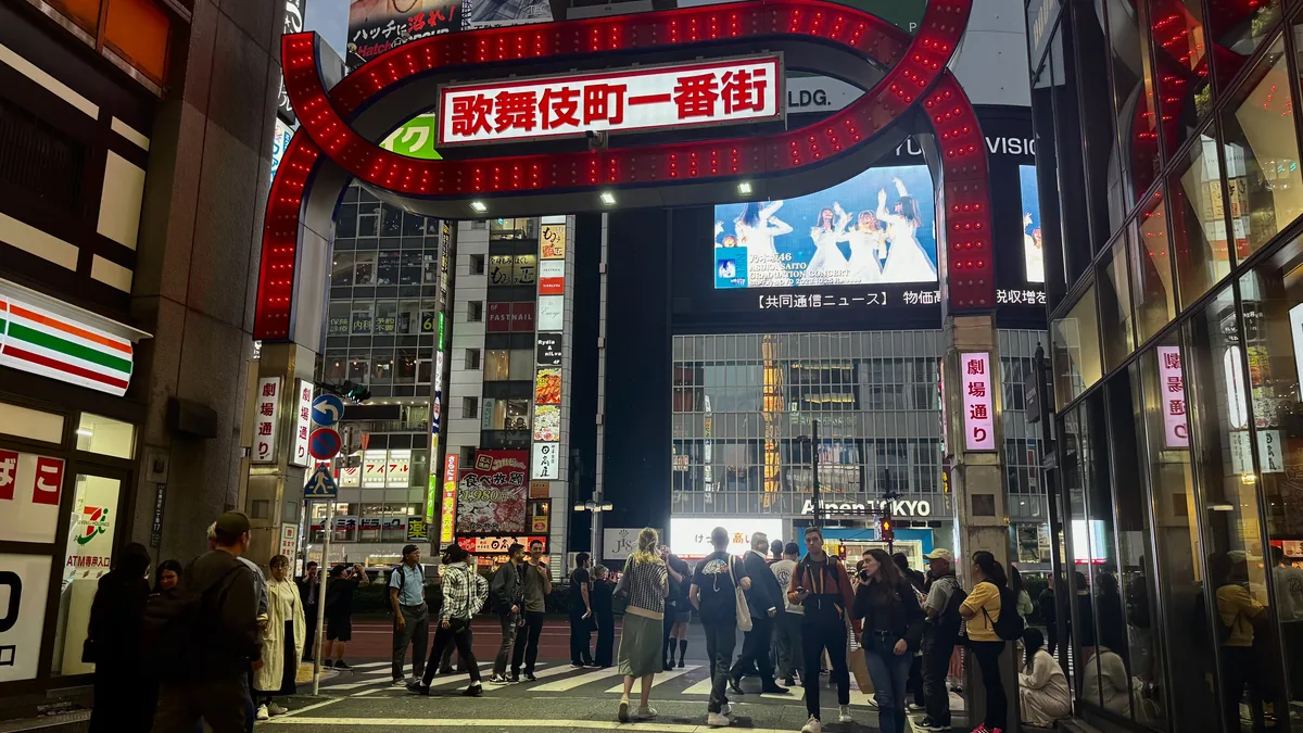 Pedestrians walking under the giant red neon Kabukicho Ichibangai sign in Tokyo at night.