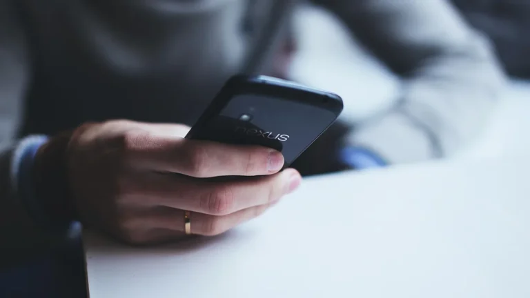 A close-up of a hand holding a black Nexus smartphone, showing the brand logo on the back of the device.