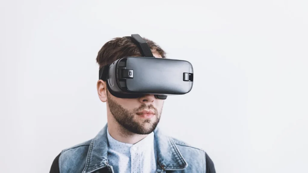 Man with beard wearing black VR headset on white background.