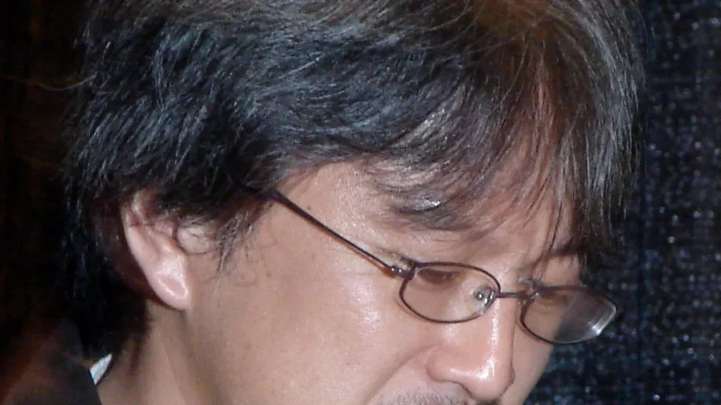 Close-up profile of video game director Eiji Aonuma wearing glasses and looking downwards.